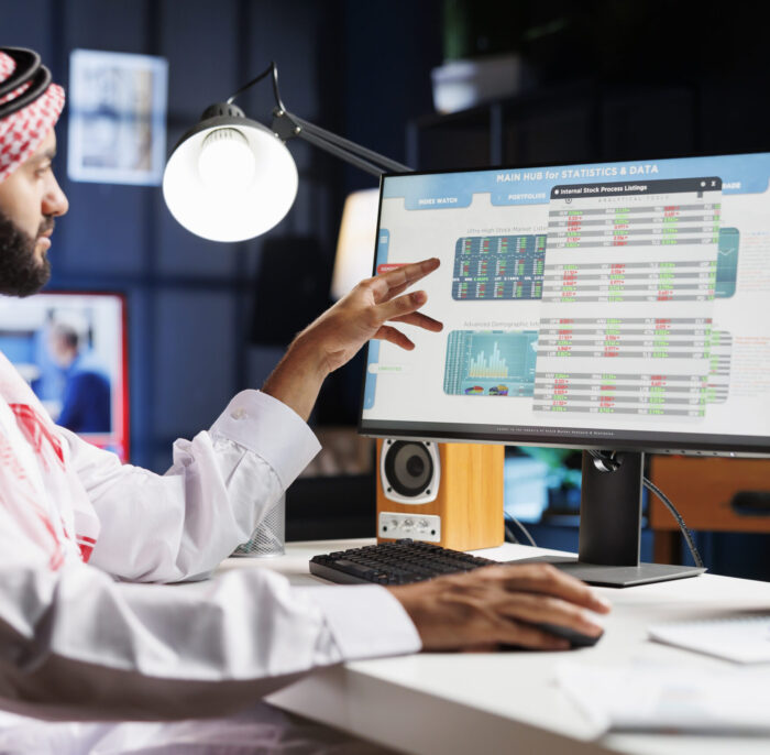 An Arab businessman diligently analyzing data on his computer, making important decisions for the company. Muslim guy wearing traditional attire is checking charts and data on his desktop pc.